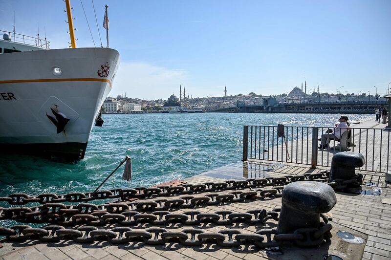 People sit on a bench next to a ferry boat at Karakoy district in front of the Galata bridge and Suleymaniye mosque in Istanbul.  AFP