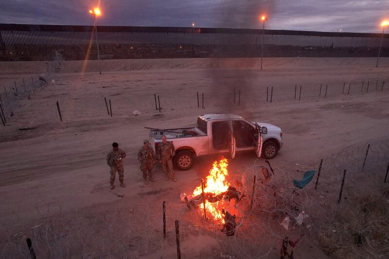 Texas National Guard members watch migrants' belongings burning on a razor wire fence at the US border, seen from Ciudad Juarez, Mexico. Reuters