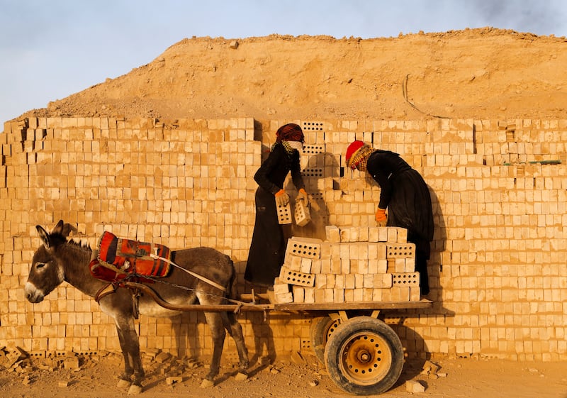 Labourers stack bricks on to a donkey-drawn cart.