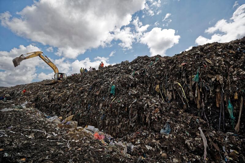 People stand next to a mechanical digger as it adds newly-dumped trash on top of a mountain of garbage at the dump in the Dandora slum of Nairobi, Kenya. AP Photo