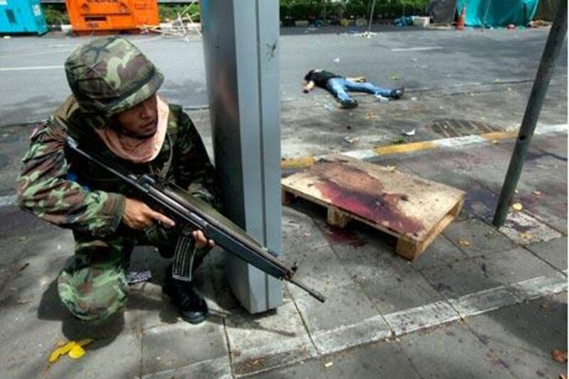 A Thai soldier takes cover near the body of a Red Shirt protester yesterday.