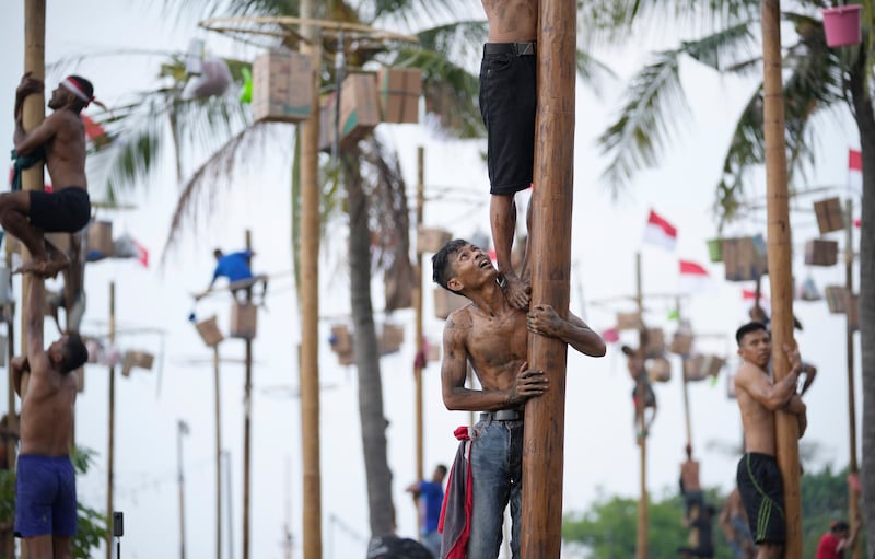 Participants try to reach the prizes during a greased-pole climbing competition held as a part of Independence Day celebrations at Ancol Beach in Jakarta, Indonesia Wednesday, Aug.  17, 2022.  Indonesia is celebrating its 77th anniversary of independence from the Dutch colonial rule.  (AP Photo / Tatan Syuflana)