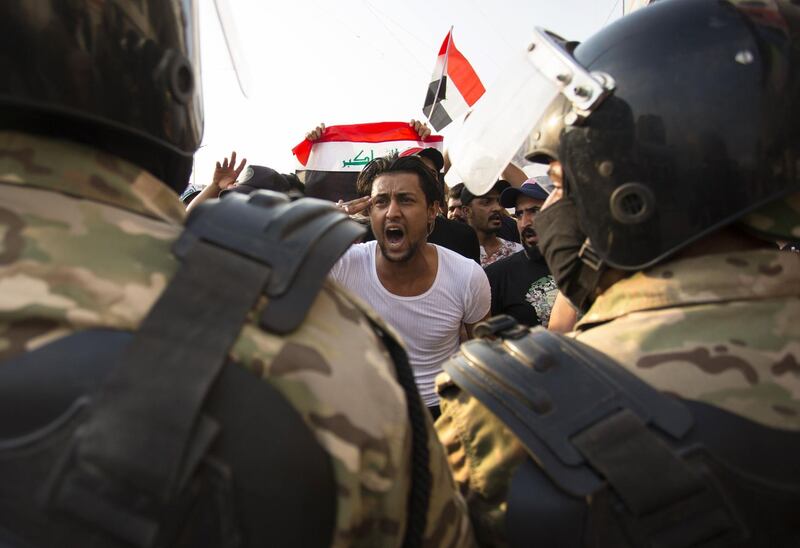TOPSHOT - An Iraqi protestor gestures in front of security forces during a demonstration against state corruption, failing public services and unemployment, on October 2, 2019 in the southern city of Basra. Popular protests multiplied across Iraq today as thousands of demonstrators braved live fire and tear gas in rallies that have left seven dead in the past 24 hours. / AFP / Hussein FALEH
