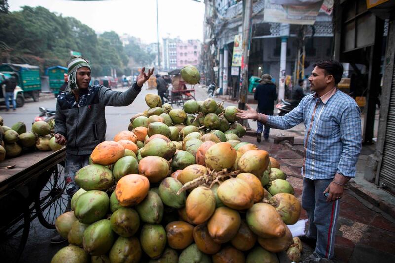 A worker passes a coconut to another man as they prepare a street stall in the old quarters of New Delhi on December 27, 2019. / AFP / XAVIER GALIANA

