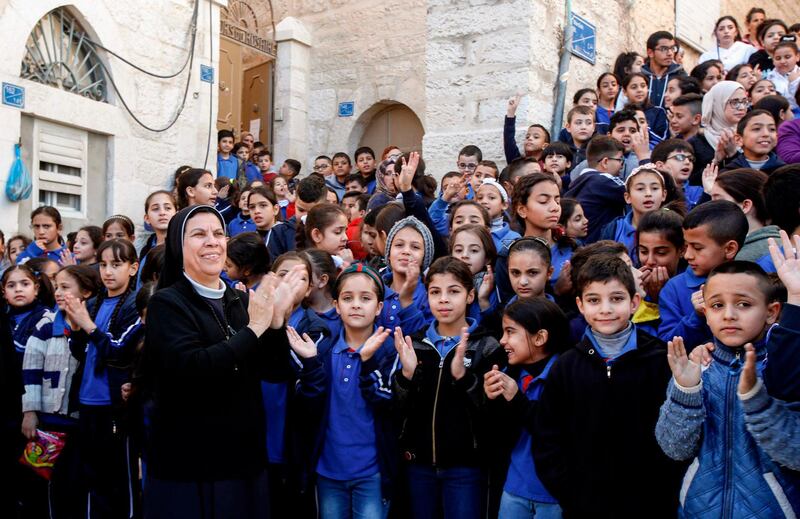 A nun claps along with Palestinian school children as they attend a parade ahead of the arrival of the relic. AFP
