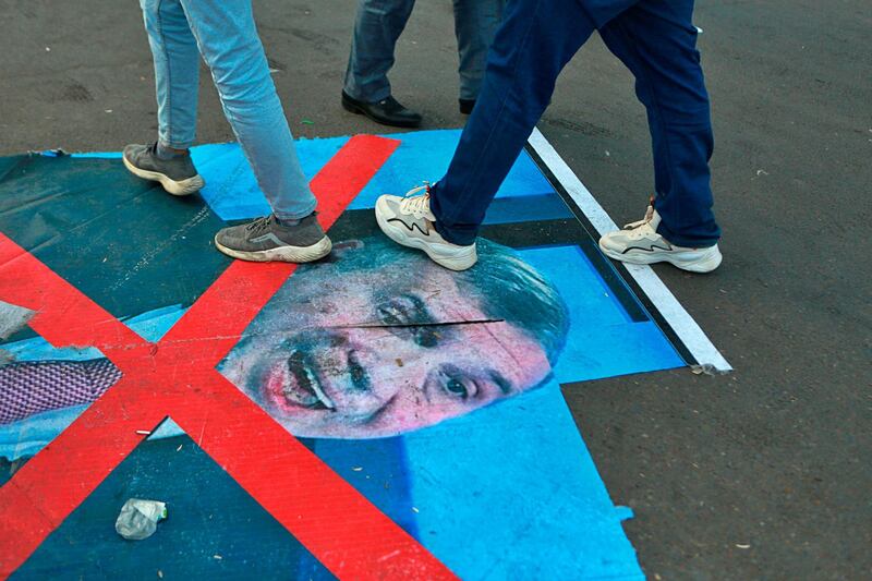 Anti-government protesters step over a defaced poster of newly-appointed Prime Minister Mohammed Allawi in Tahrir Square, Baghdad, Iraq. AP Photo