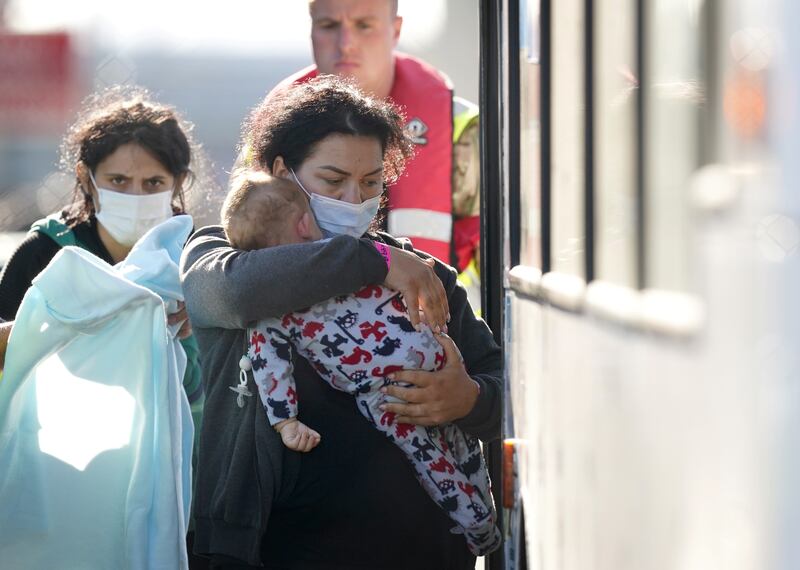 A lady carries a toddler to a bus after a group of people thought to be migrants were brought in to Dover, Kent, on the south-east English coast. PA