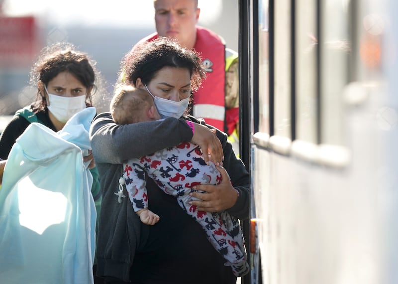 A lady carries a toddler to a bus after a group of people thought to be migrants were brought in to Dover, Kent, on the south-east English coast. PA