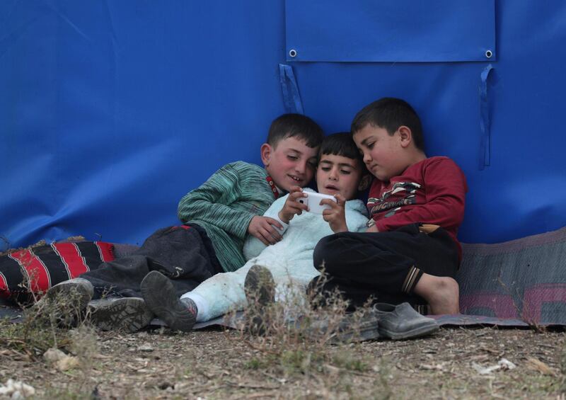 Internally displaced Syrian boys play on a mobile phone outside a tent in Azaz, Syria. REUTERS
