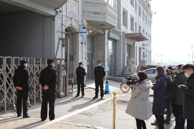 Journalists film as security officers stand guard at an entrance to a court building in Dandong in northeastern China's Liaoning Province, Friday, March 19, 2021. China was expected to open the first trial Friday for Michael Spavor, one of two Canadians who have been held for more than two years in apparent retaliation for Canada's arrest of a senior Chinese telecom executive. (AP Photo/Ken Moritsugu)