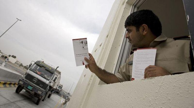 Tollgate officer Hussain Ahmed Mohammed prepares to hand a brochure to a lorry driver that explains the route and fees for travelling on the new toll road near Al Dhaid. The toll starts today.