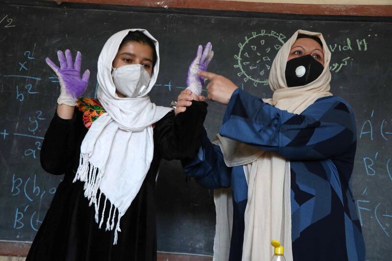 A teacher demonstrates to children how to protect themselves against the coronavirus at a school in Herat, Afghanistan, as centres of learning reopened.  EPA