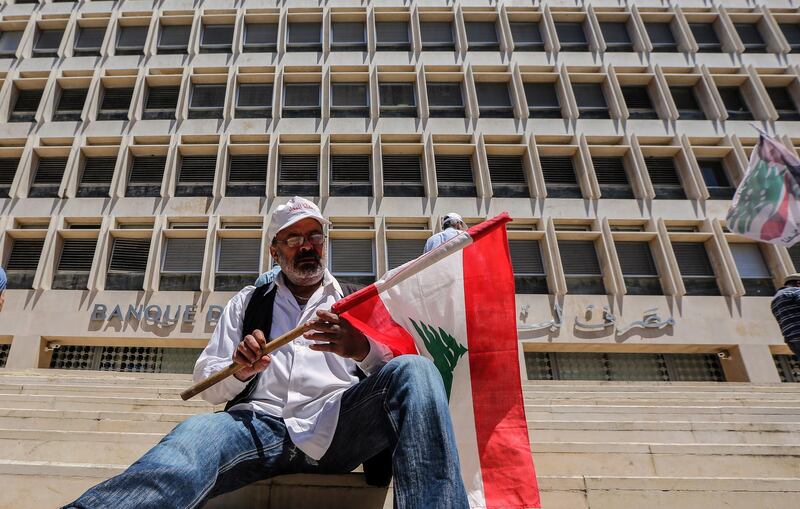 epaselect epa07567203 Retired army officer carries a Lebanese flag and sits in front of the Lebanese Central Bank during the protest in Hamra Street in Beirut, Lebanon, 13 May 2019. According to media reports, the protesters blocked entrances to the Lebanese Central Bank and the Banks street as a preemptive strike against any austerity measures in the 2019 draft. General Sami Ramah, a representative for the retired soldiers, said they would stay at the bank, stopping employees from entering, till their request of no cuts to the military budget was met.  EPA/Nabil Mounzer