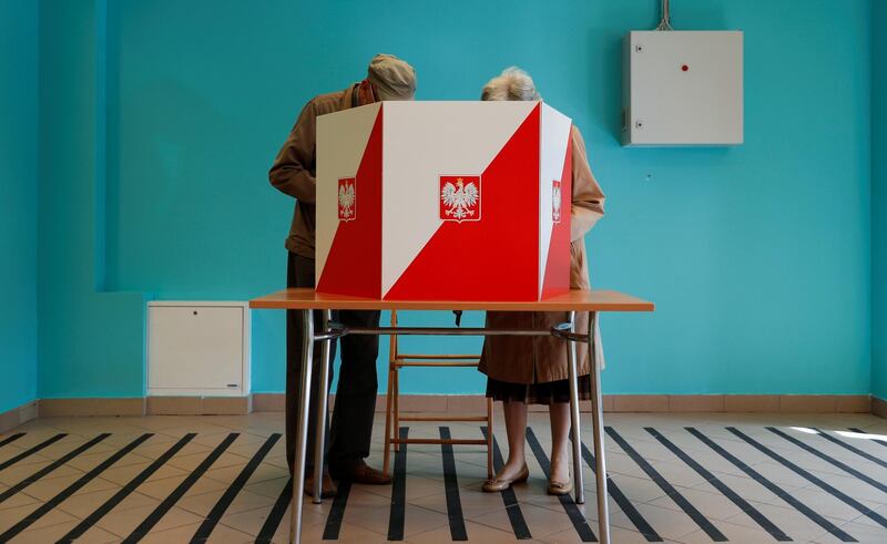 People stand next to a voting booth during the second round of the presidential election at a polling station in Warsaw, Poland. Reuters