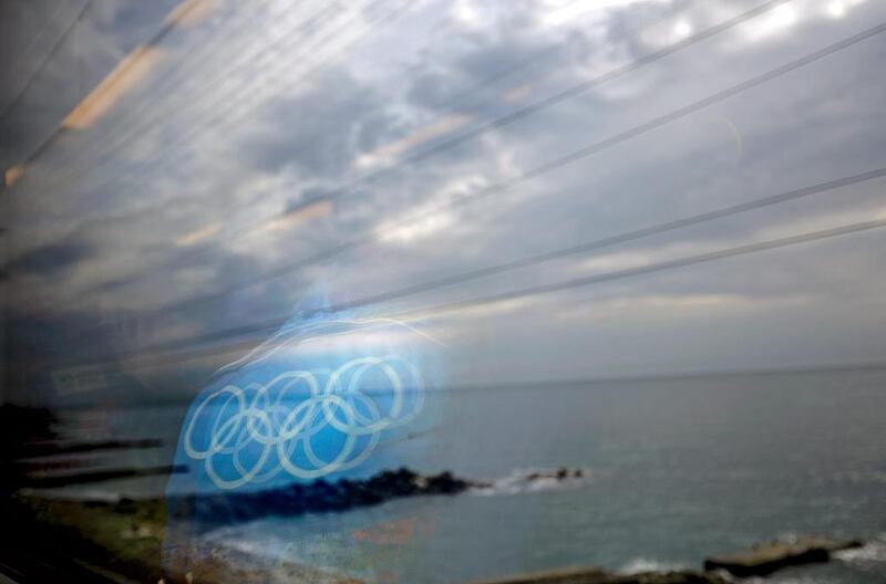 The Olympic rings on the back of a jacket of a worker are reflected in a train window as it travels from the Olympic Park to the Sochi city center along the Black Sea in Sochi. David Goldman / AP