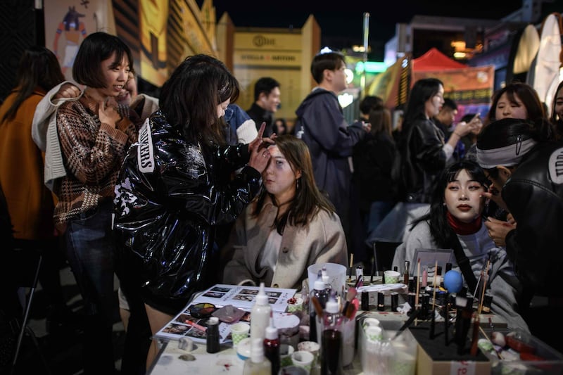 Revellers apply Halloween make-up as they sit on a street in the popular nightlife district of Itaewon in Seoul.  AFP