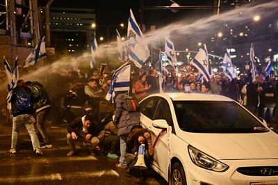 People shelter behind a car as Israeli police use water cannons against anti-government protesters in Tel Aviv on February 24. Reuters