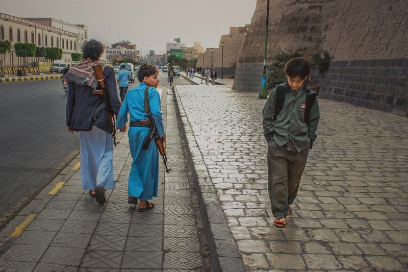 A young boy carrying an AK-47 looks over his shoulder at a boy of a similar age carrying a back-pack, showing the starkly different futures ahead of Sanaa's young generation of children.Ali Alsonidar