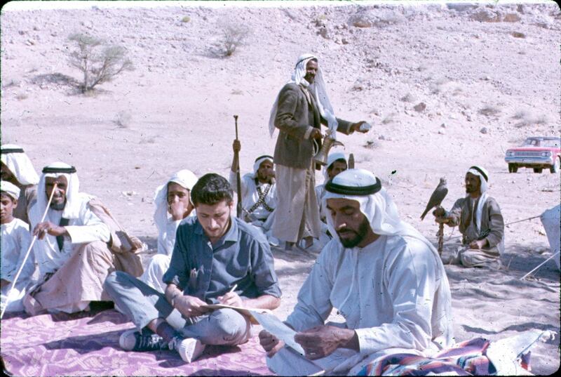 The Founding President Sheikh Zayed, sits in the desert with an unidentified translator at his right. This was taken during one of JB Kelly's trips to Abu Dhabi around 1964. Note the classic car at top right.