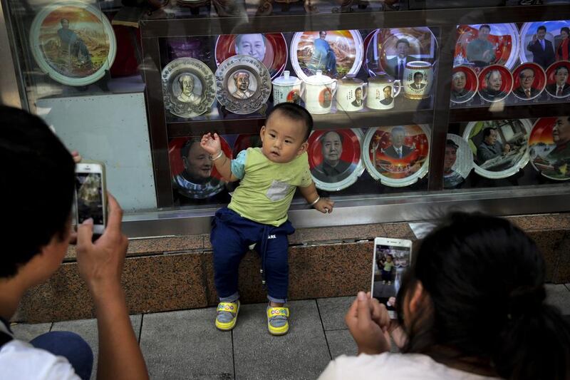 A couple take snaps on September 9, 2016,  of their child posing near souvenir plates and cups bearing images of the late communist leader Mao Zedong at a shop near Tiananmen Square in Beijing. Friday marks the 40th anniversary of the death of Mao Zedong, who founded the People's Republic of China in 1949, and ran it virtually uncontested until his death on September 9, 1976. Andy Wong / Associated Press