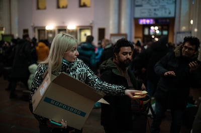 A volunteer hands out sandwiches as hundreds of people cram into the ticket hall at the main railway station in Lviv hoping to get onto a train out of Ukraine. Oliver Marsden for The National