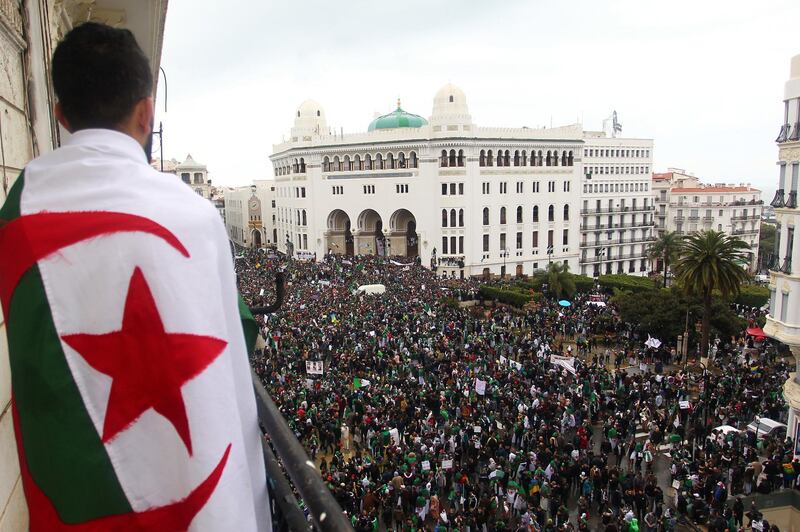 An Algerian man draped in a national flag watches as protesters gather for a demonstration against ailing President Abdelaziz Bouteflika in front of La Grande Poste (main post office) in the centre of the capital Algiers on March 22, 2019. - Bouteflika said on February 22 he would run for a fifth term in April 18 elections, despite concerns about his ability to rule. The 82-year-old uses a wheelchair and has rarely appeared in public since suffering a stroke in 2013. Following initial protests, he made the surprise announcement on March 11 that he was pulling out of the race -- and also postponed the polls. (Photo by - / AFP)
