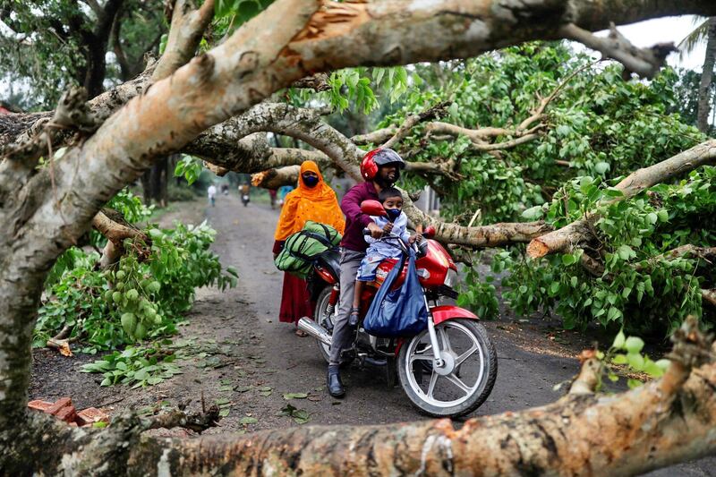 A man with a child ride on motorbike in the street blocked by trees that were uprooted by the cyclone Amphan, in Satkhira, Bangladesh. REUTERS