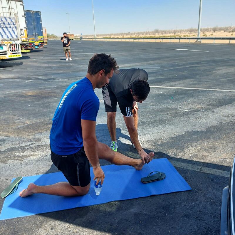 A member of his support team helps him stretch by the side of the road on a particularly hot afternoon after his hamstrings seized up.