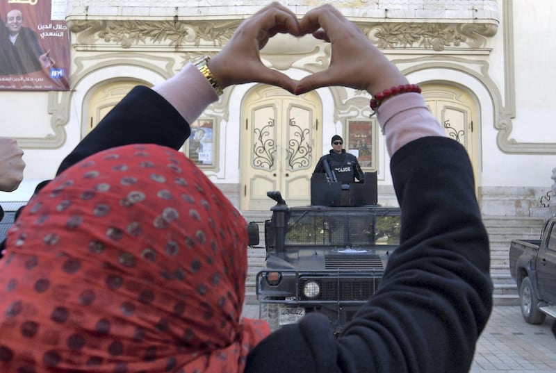 A Tunisian woman makes a heart sign as she stands in front of security forces guarding the area during a rally marking the ninth anniversary of the 2011 uprising on Habib Bourguiba Avenue in central Tunis on January 14, 2020. (Photo by FETHI BELAID / AFP)