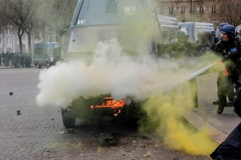 French riot police try to extinguish a fire on their van during clashes with yellow-vest protesters on the Champs-Elysees. AF