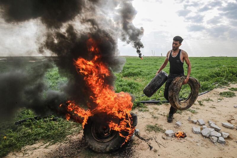 A Palestinian man sets fire to tyres along the Gaza-Israel border east of Khan Yunis in the southern Gaza Strip. Israeli forces shot dead a Palestinian before extracting his body with a bulldozer.  AFP