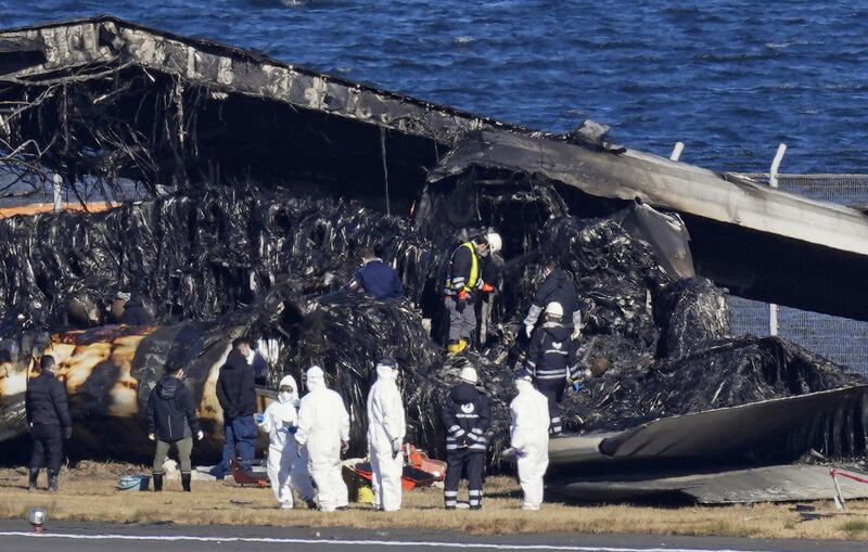 Officials inspect the wreckage of the Japan Airlines passenger plane at Haneda Airport in Japan. AP