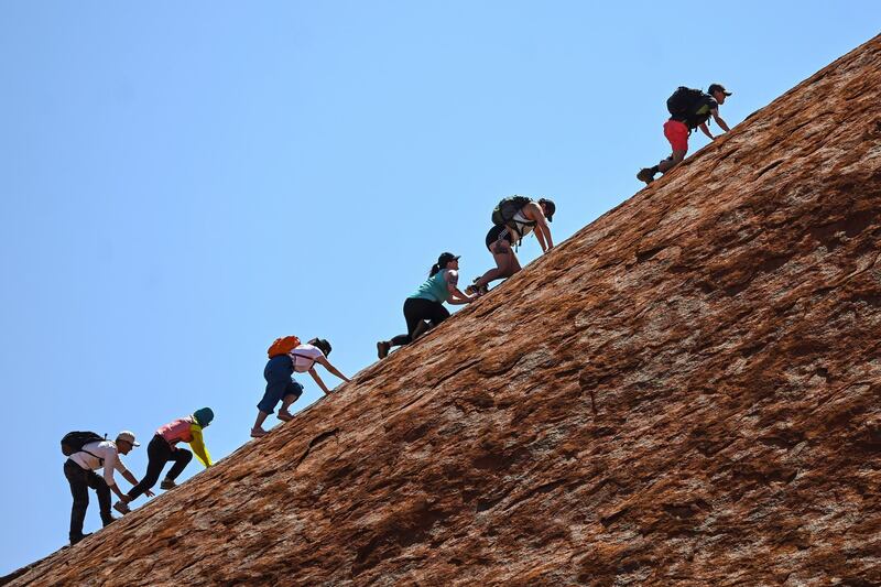 Tourists climb the sandstone monolith called Uluru that dominates Australia's arid center at Uluru-Kata Tjuta National Park. AAP Image via AP
