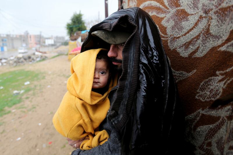 A Palestinian man stands outside with a child on a rainy day in Khan Younis, southern Gaza Strip, on January 16. Reuters