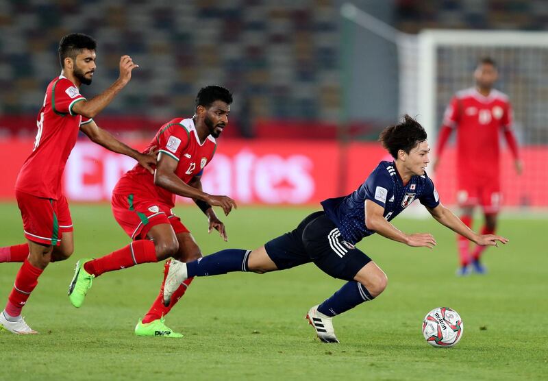 Abu Dhabi, United Arab Emirates - January 13, 2019: Minamino Takumi of Japan is tripped by Ahmed Al Mahaijri (M) and Salaah Al Yahyaei of Oman during the game between Japan and Oman in the Asian Cup 2019. Sunday, January 13th, 2019 at Zayed Sports City Stadium, Abu Dhabi. Chris Whiteoak/The National