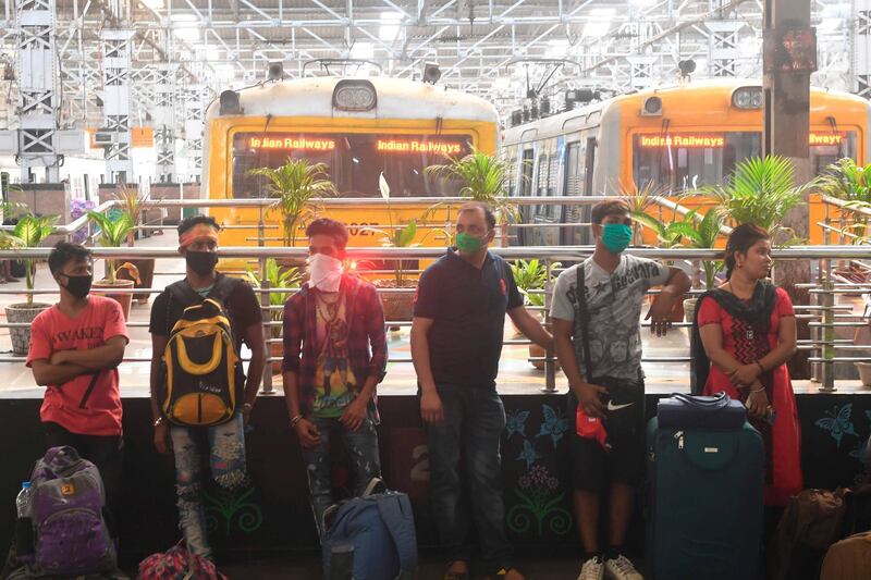 Passengers wearing facemasks wait to board a train at a railway station in Kolkata.  AFP