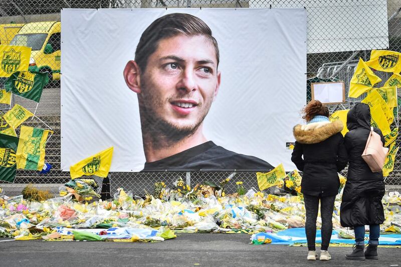 (FILES) In this file photo taken on February 08, 2019 People look at yellow flowers displayed in front of the portrait of Argentinian forward Emiliano Sala at the Beauvoir stadium in Nantes, on February 8, 2019.  The plane carrying footballer Emiliano Sala that crashed in the Channel last month did not have a commercial licence, British investigators said on February  25, 2019. / AFP / LOIC VENANCE
