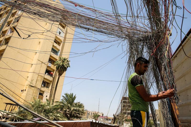 A man checks the wiring on electric cables reaching out to homes in Saadoun Street in the Iraqi capital Baghdad on July 29, 2018, as chronic power shortages have forced residents to buy electricity from private entrepreneurs who run generators on street corners across the country. - Iraqi Prime Minister Haider al-Abadi sacked his minister of electricity on July 29 after three weeks of protests against corruption and chronic power cuts in the energy-rich country where successive conflicts have devastated infrastructure. (Photo by SABAH ARAR / AFP)