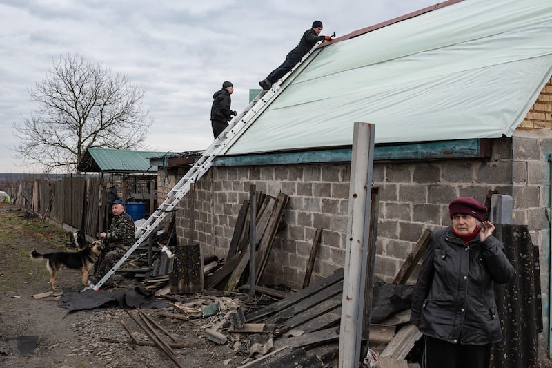 A man repairs the roof of a house while standing on a ladder, in Andriivka, Ukraine. Getty Images