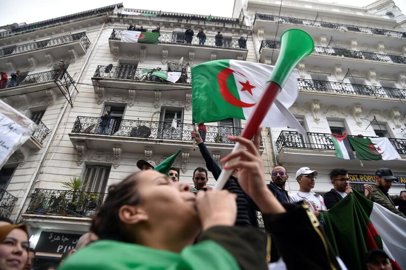 (FILES) In this file photo taken on March 22, 2019 An Algerian woman blows a vuvuzela with the national colours as others wave national flags during a demonstration against ailing President Abdelaziz Bouteflika in the capital Algiers. Every Friday, the first day of the weekend in Algeria, protesters invade the streets. The events were hailed for their organization, pacifism, humor and signs, but also for their festive side. Too festive for some that music and dances irritate. / AFP / RYAD KRAMDI                        
