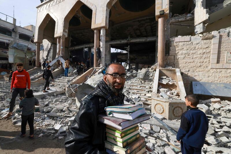 A man walks with salvaged religious books as people inspect the damage to a mosque in Rafah following Israeli bombardment. AFP