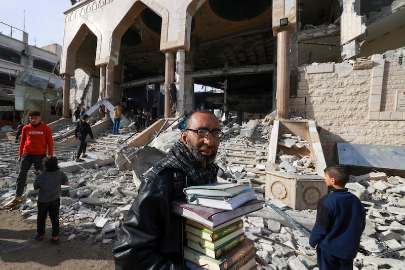 A man walks with salvaged religious books as people inspect the damage to a mosque in Rafah following Israeli bombardment. AFP