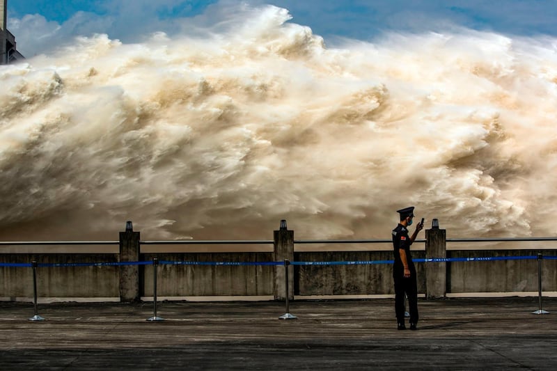 This photo taken on July 19, 2020 shows a security guard looking at his smartphone while water is released from the Three Gorges Dam, a gigantic hydropower project on the Yangtze river, to relieve flood pressure in Yichang, central China's Hubei province. Rising waters across central and eastern China have left over 140 people dead or missing, and floods have affected almost 24 million since the start of July, according to the ministry of emergency management. - China OUT
 / AFP / STR
