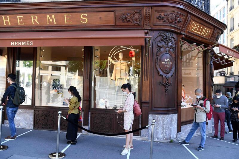 (FILES) In this file photograph taken on May 20, 2020, customers wear protective face masks respect social distancing measures as they queue in front of the Hermes store on George V Avenue in Paris, after France eased then lockdown measures taken to curb the spread of the coronavirus (Covid-19)pandemic. Stock prices for luxury group Hermes rose more than 5% on early February 19, 2021, on the Paris Stock Exchange, following the publication of annual results that were resilient in the face of the coronavirus pandemic thanks to a rebound in sales in Asia in the second half of the year. / AFP / ALAIN JOCARD
