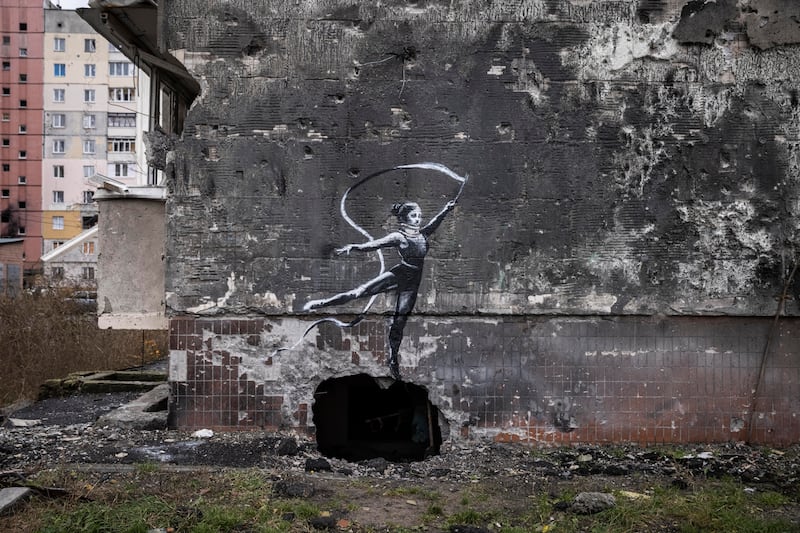 A gymnast in a leotard and wearing a neck brace waves a ribbon on the wall of a destroyed building in Irpin. Getty