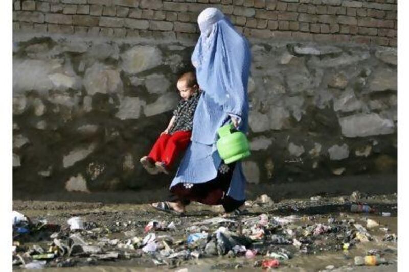A  woman swings her child over a drain as she carries a gas fuel canister, in Kabul, Afghanistan, the country with the world's worst record for maternal health.