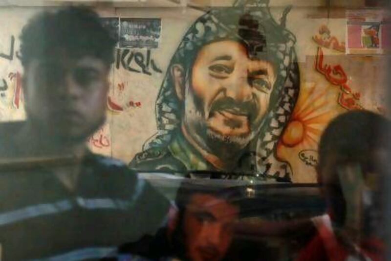 Palestinians with a mural depicting their late leader Yasser Arafat are reflected in a shop window in Gaza City. New suspicions that Arafat was murdered have prompted calls for a medical examination of his remains.