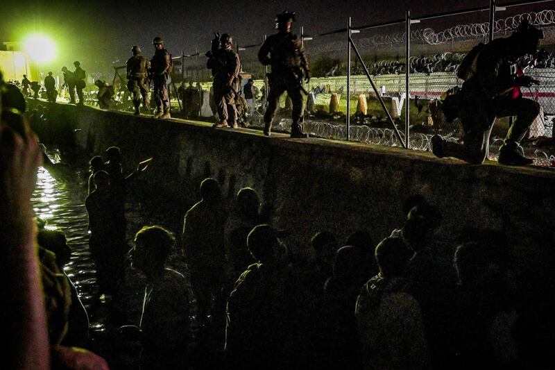 British and Canadian soldiers stand guard near a canal as Afghans wait outside the foreign military-controlled part of the airport in Kabul.  AFP