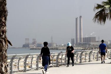 People walk on the seaside promenade with the floating Turkish power station Karadeniz Powership Fatmagul (L) seen in the background next to Lebanon's Zouk Mosbeh power plant, north of the capital Beirut, on April 9, 2019. 
