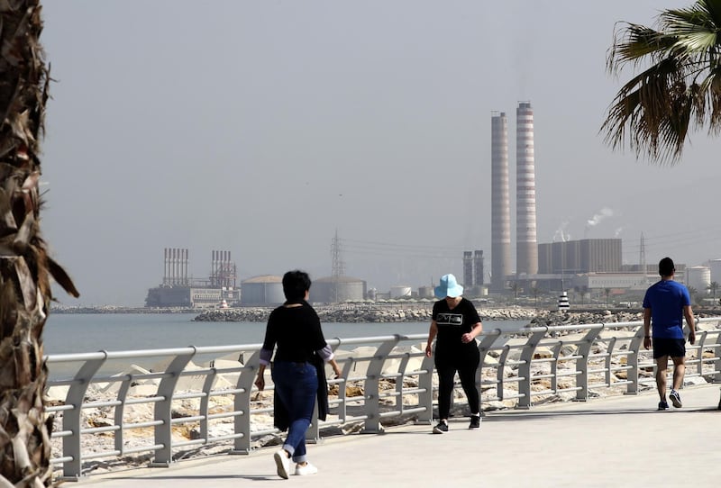 People walk on the seaside promenade with the floating Turkish power station Karadeniz Powership Fatmagul (L) seen in the background next to Lebanon's Zouk Mosbeh power plant, north of the capital Beirut, on April 9, 2019. The Lebanese cabinet has approved a plan to restructure the country's ailing electricity sector vowing to provide power 24 hours a day from a grid notorious for blackouts. / AFP / JOSEPH EID
